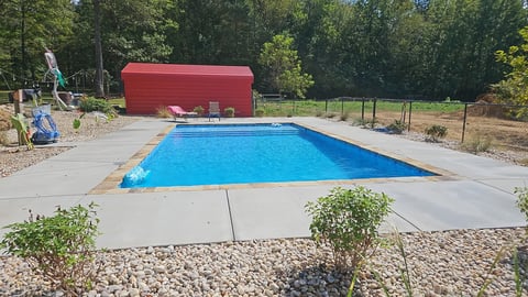 Backyard swimming pool with bright blue water surrounded by concrete patio